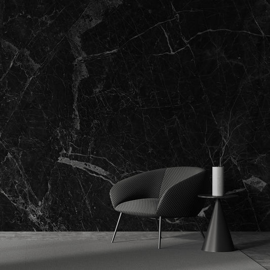 A modern living room with a black marble wall featuring a contemporary chair and a cylindrical table with a white lamp.